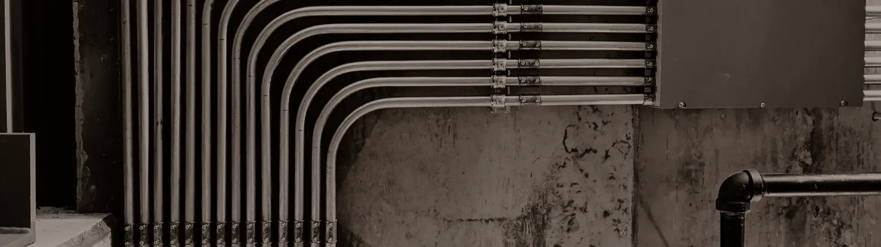 A run of steel conduit bent along a bare concrete wall